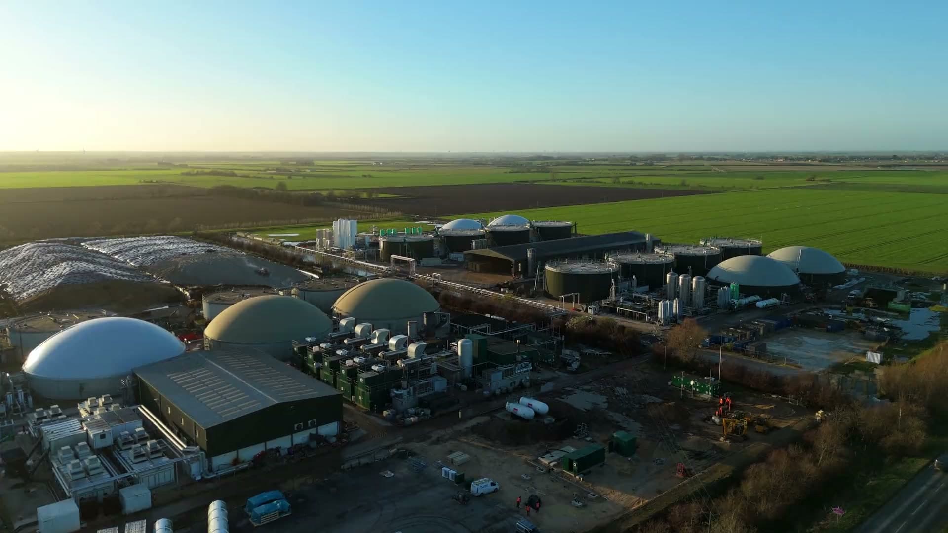 Planta de biogás en operación, vista aérea al amanecer entre campos de cultivo